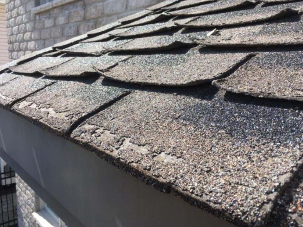 Bardeaux d'asphalte sur une toiture retroussés à cause de la délamination et de l'usure avancée